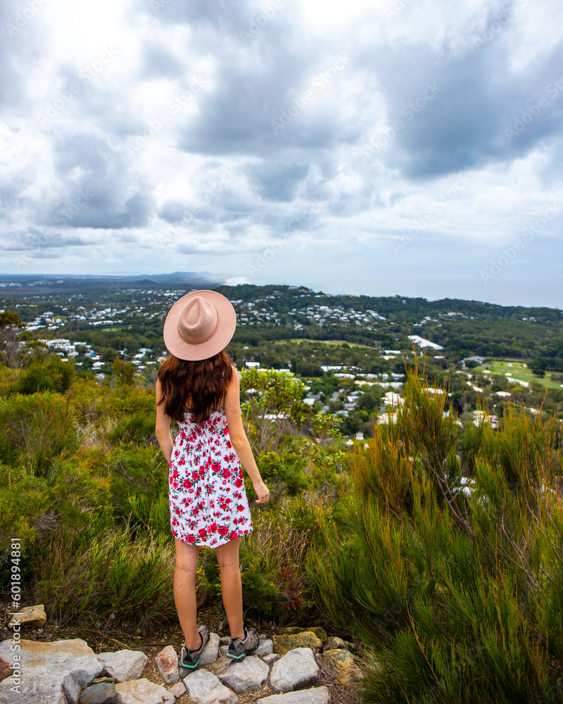 beautiful woman in colorful dress and elegant hat watching panorama of coolum beach and sunshine coast from the top of mount coolum, queensland, australia
