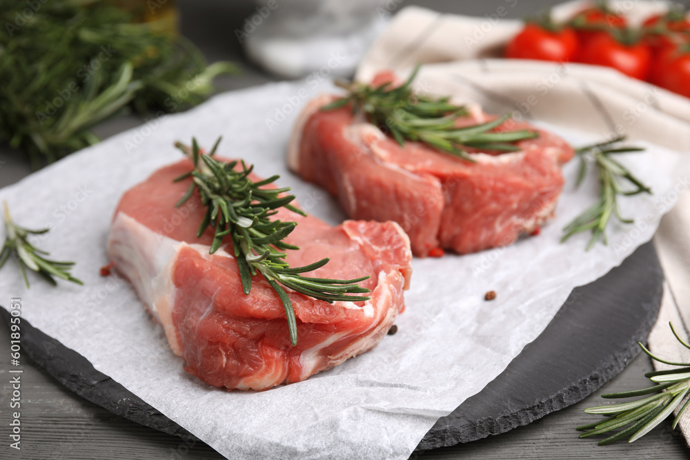 Fresh raw meat with rosemary on grey wooden table, closeup