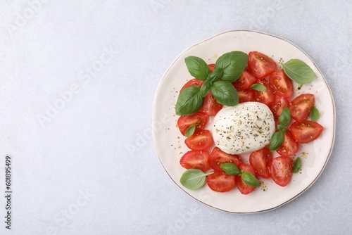 Tasty salad Caprese with mozarella, tomatoes and basil on light table, top view. Space for text