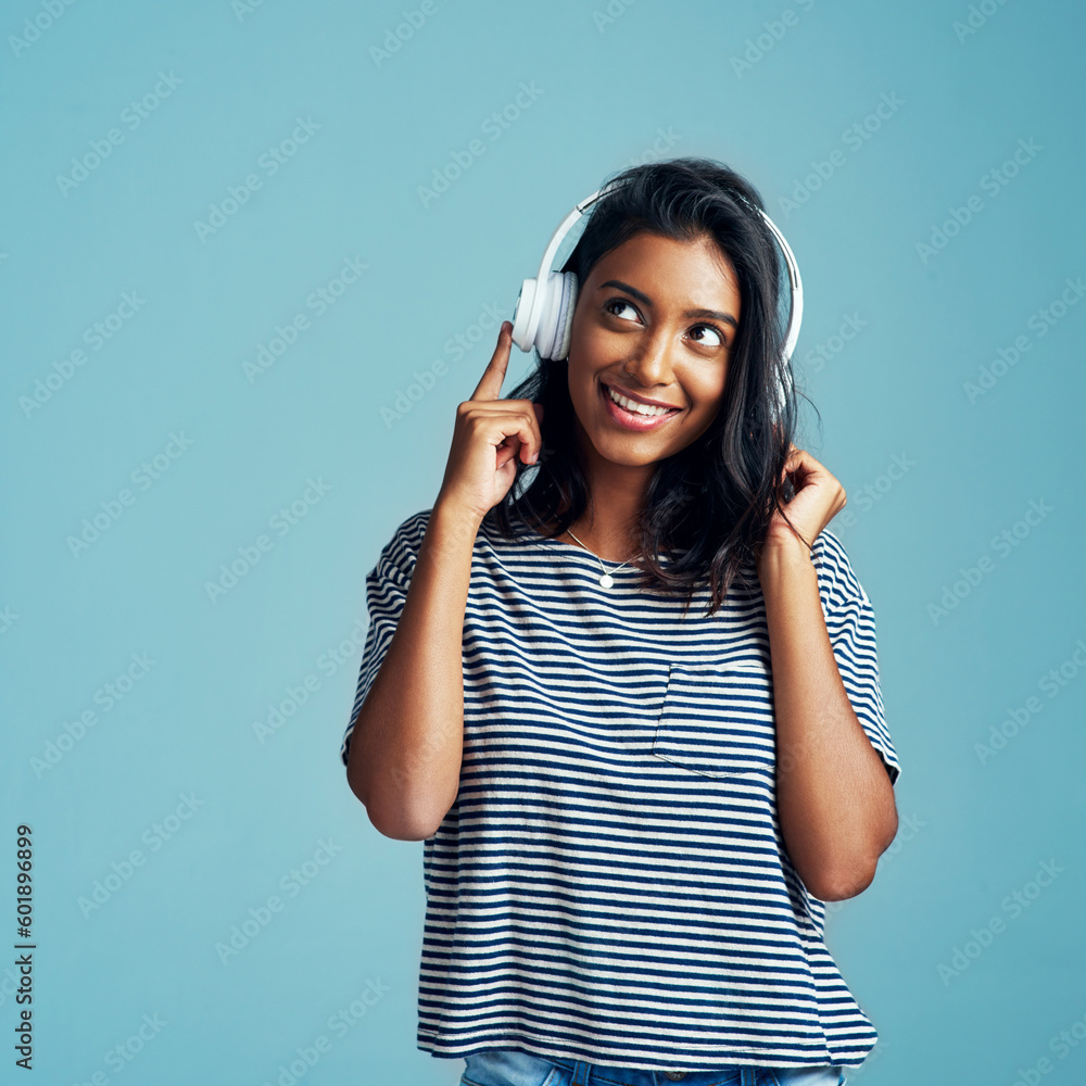 Woman, thinking and headphones with music in studio with happiness and web audio. Blue background, Indian female person and young model listening, hearing and streaming a song with smile and mockup - obrazy, fototapety, plakaty 