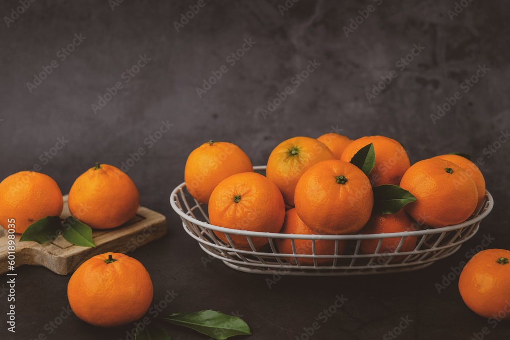Orange fruit with green leaves on the Mandarin or Tangerine oranges in the basket on the stone table. Still life
