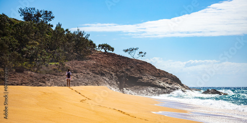 lonely woman walking on the sand dunes towards large cliff made of red rocks; walking alone on australian beach near agnes water in queensland, australia photo