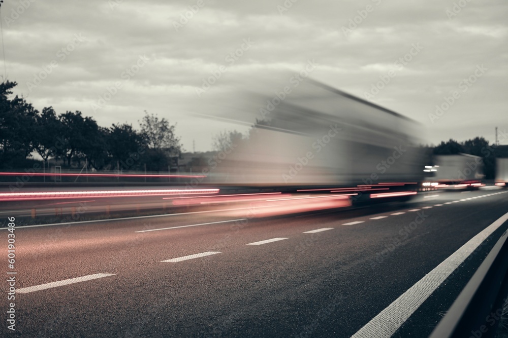 A truck driving on the highway at dusk. Motion blur on the highway. Evening shot of a truck. Concept of international transport and logistics. Almost monochrome image.