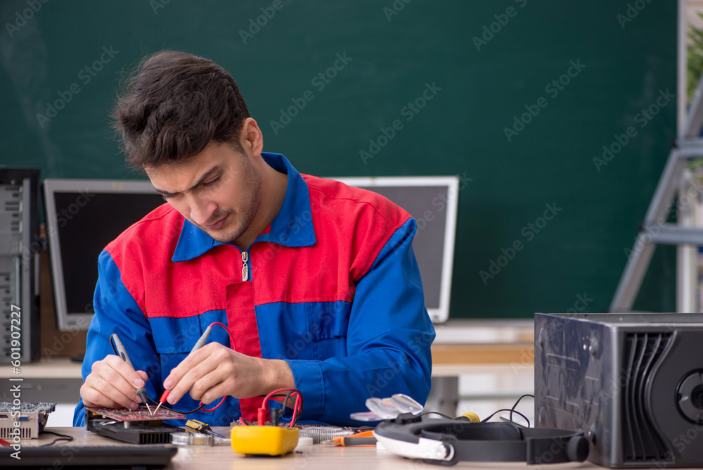 Young male repairman repairing computers in the classroom Young male repairman repairing computers in the classroom