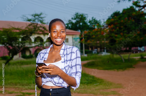 beautiful young african lady smiling while using her phone outdoors
