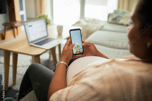 Young pregnant latina woman using a diet app on her smart phone while sitting on a couch in the living room of her home