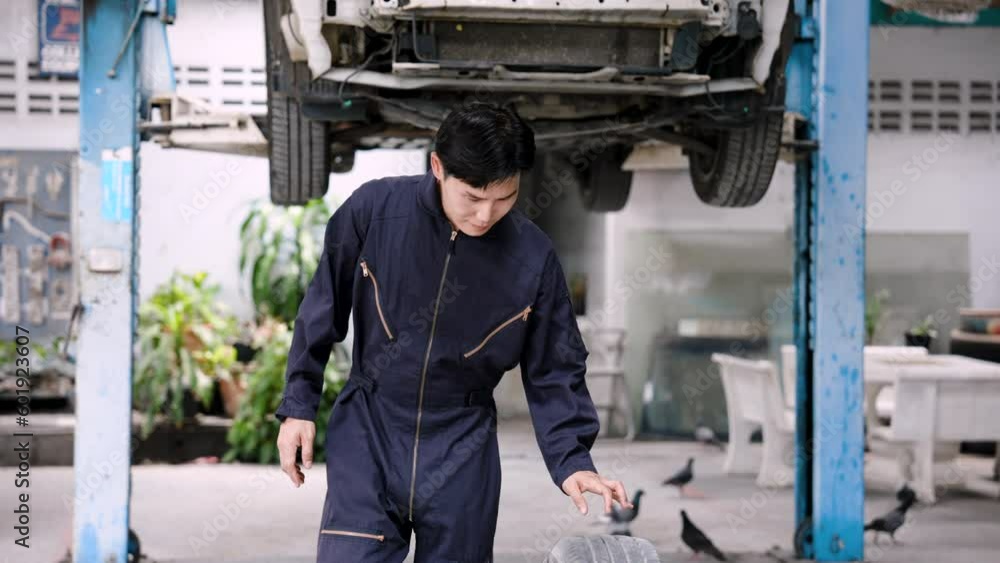 Asian male car repairman rolling a car tire. by skilled mechanics to change all 4 tires to put the car parked waiting to be repaired in the garage in order to return to use Asian male car repairman rolling a car tire. by skilled mechanics to change all 4 tires to put the car parked waiting to be repaired in the garage in order to return to use