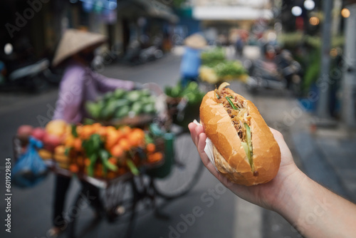Street food in Hanoi. Hand holding Banh Mi sandwich. Close-up of traditional Vietnamese baguette filled with pate, meat and vegetables..