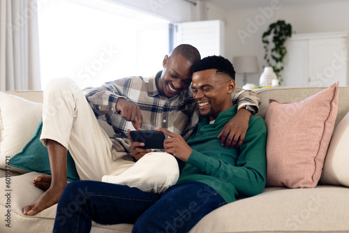 Smiling african american gay couple browsing social media on smart phone while relaxing on sofa photo