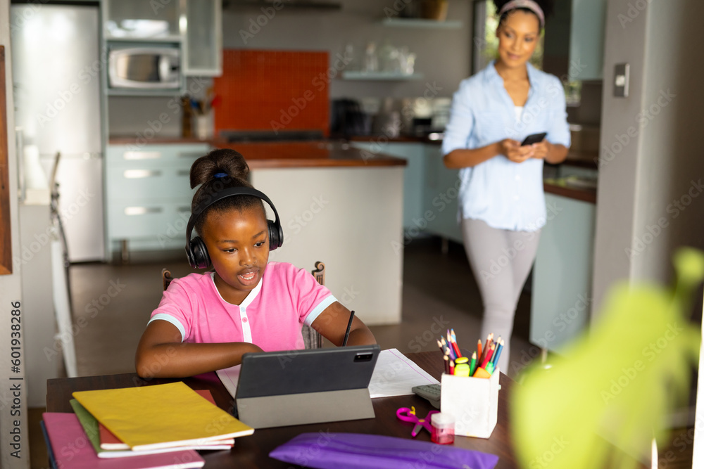 Happy african american mother watching daughter in headphones having online lesson on tablet at home Happy african american mother watching daughter in headphones having online lesson on tablet at home
