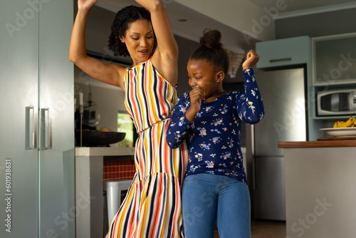 Happy african american mother and daughter having fun dancing together in kitchen photo