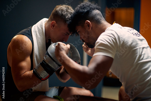 Young boxing player with coach in dressing room preparing for workout, holding heads against each other.