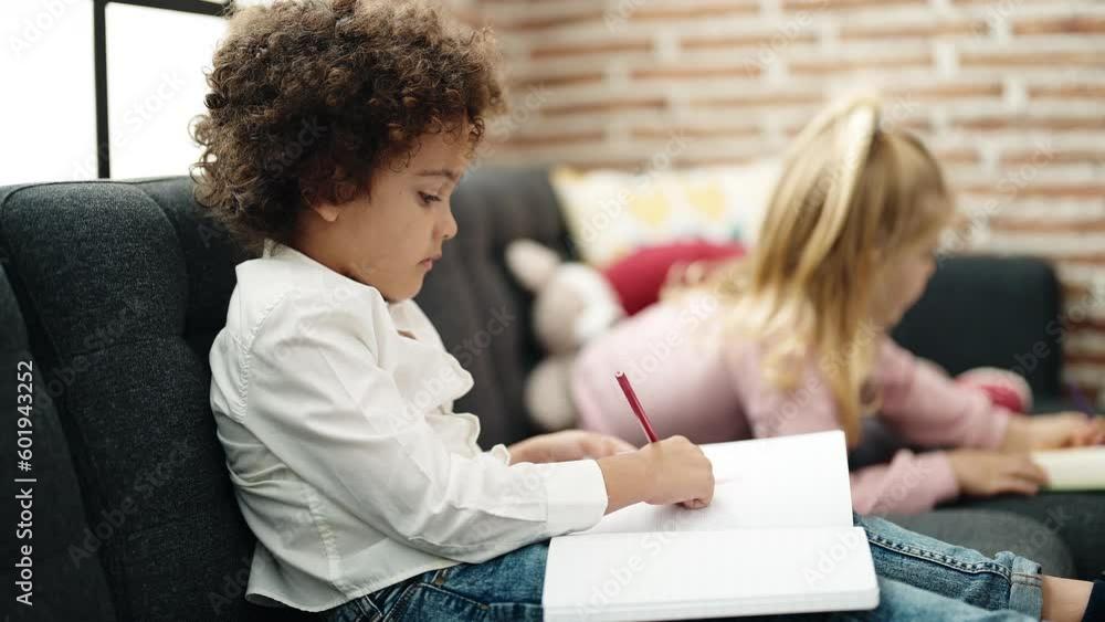 Adorable boy and girl students sitting on sofa drawing on notebook at home Adorable boy and girl students sitting on sofa drawing on notebook at home