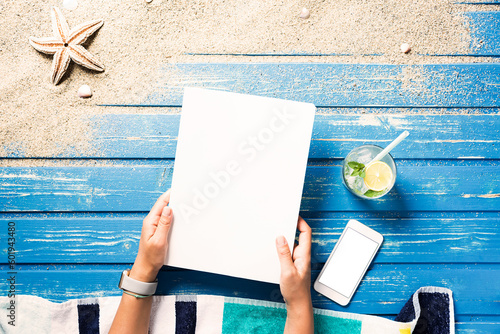 Woman hands holding white blank magazine cover mockup on beach towel