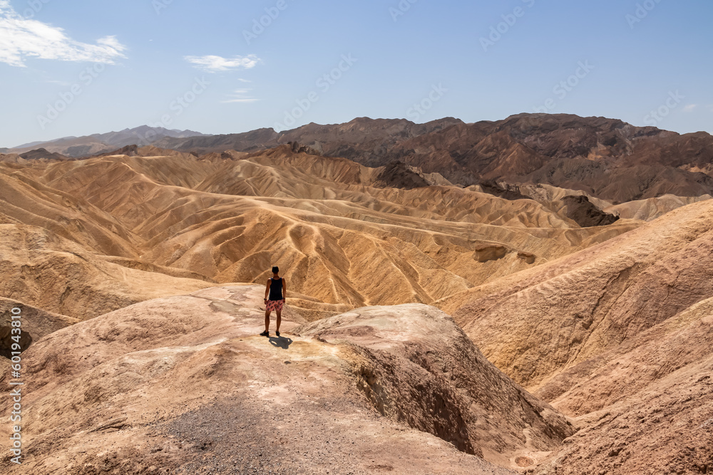 Man with scenic view Badlands of Zabriskie Point, Furnace creek, Death Valley National Park, California, USA. Erosional landscape of multi hued Amargosa Chaos rock formations, Panamint Range in back