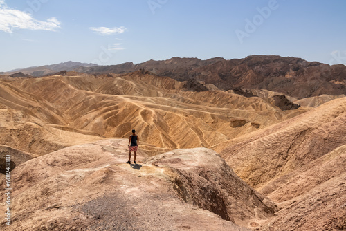 Man with scenic view Badlands of Zabriskie Point, Furnace creek, Death Valley National Park, California, USA. Erosional landscape of multi hued Amargosa Chaos rock formations, Panamint Range in back photo