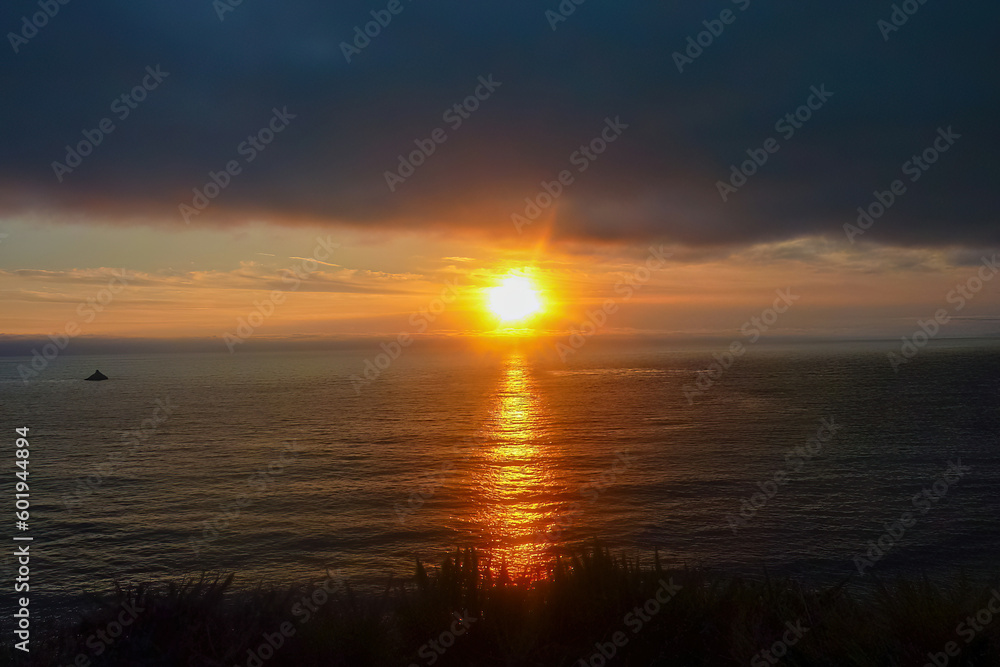 Watching sunset from Bixby Creek Bridge on coastline of Big Sur, Monterey county, California, USA, America. View of horizon of Pacific Ocean. Sun is reflecting in calm sea. Vibrant clouds in the sky