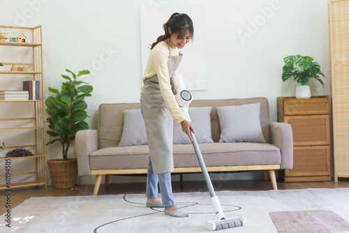 Maid using cordless vacuum cleaner to vacuuming and cleaning the dust on the carpet in home