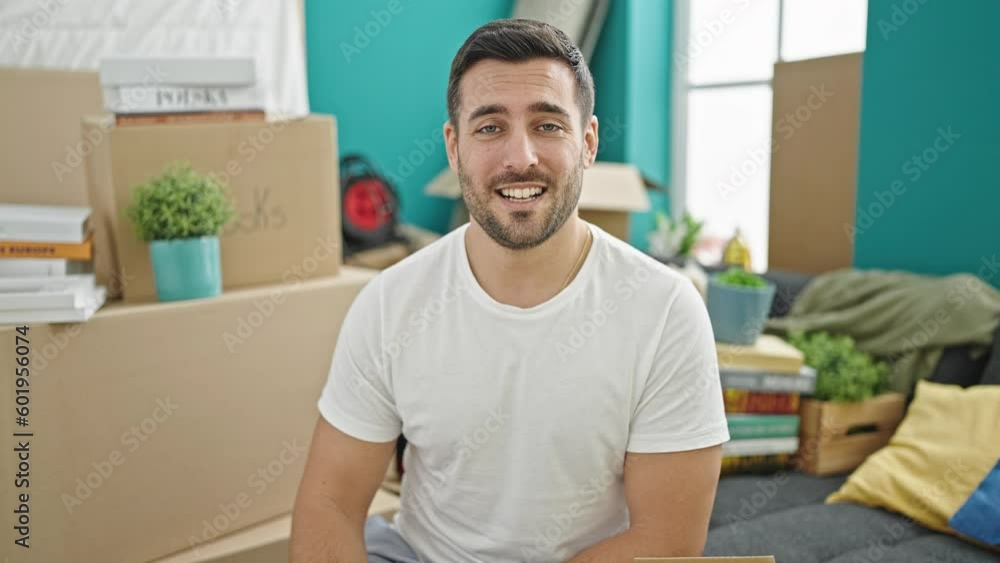 Young hispanic man holding new house keys sitting on sofa speaking at new home Young hispanic man holding new house keys sitting on sofa speaking at new home