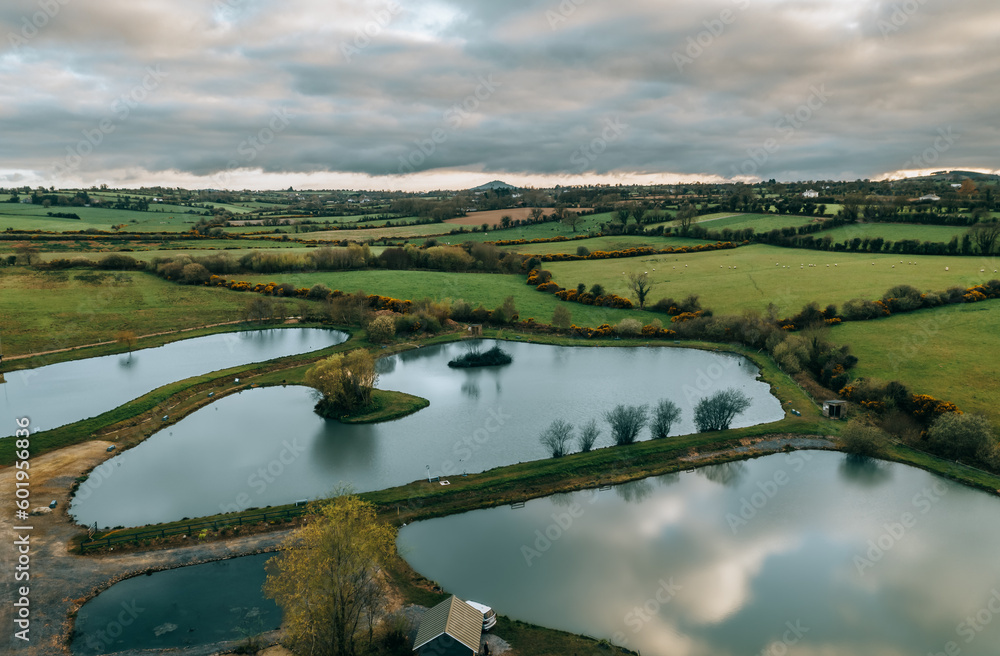 Enjoy the tranquil beauty of an Irish fishing lake at sunset in this stunning aerial photograph, with reflections of trees on the calm waters.