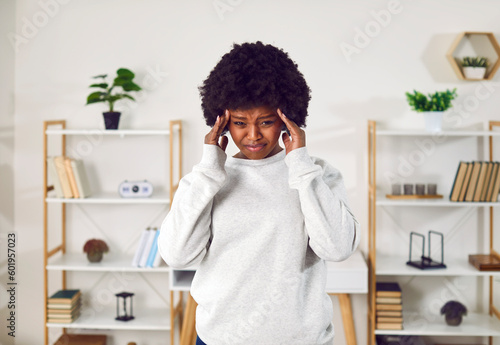 Portrait of a sad, frustrated woman with tears in her eyes. Young African American girl standing in the living room, holding her head and crying with a very sad, upset, distressed face expression