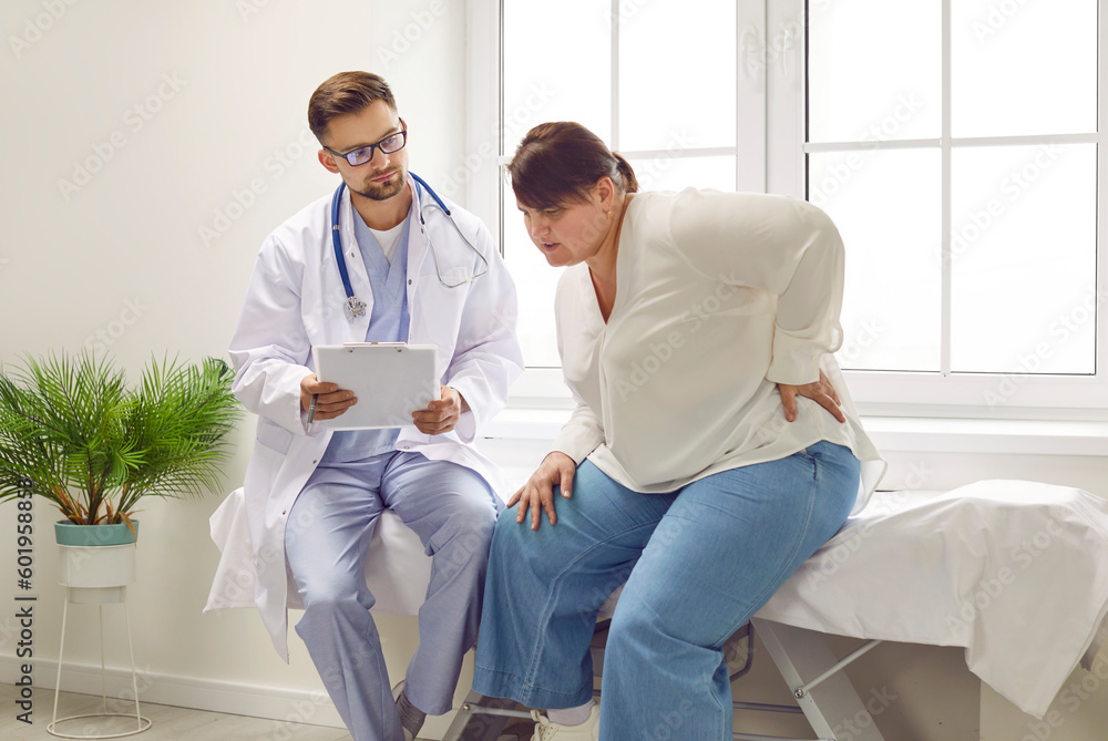 Fat young plump overweight woman sitting on the couch at the medical examination in the doctor's office suffering from backache. Obesity problems, rheumatism and healthcare concept. Fat young plump overweight woman sitting on the couch at the medical examination in the doctor's office suffering from backache. Obesity problems, rheumatism and healthcare concept.