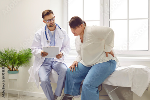 Fat young plump overweight woman sitting on the couch at the medical examination in the doctor's office suffering from backache. Obesity problems, rheumatism and healthcare concept.