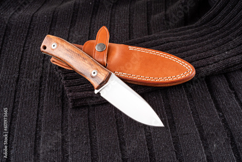 Knife with a fixed blade. Knife and leather sheath. Knife against the background of a knitted black sweater.