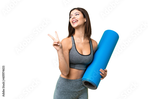 Young sport woman going to yoga classes while holding a mat over isolated chroma key background smiling and showing victory sign
