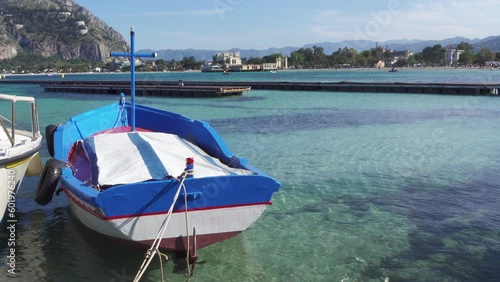 Sicily, small boat in a beautiful transparent turquoise blue sea water in summer moored in Mondello bay, Palermo, Sicily, Italy. View from the small port of the holiday resort of Mondello. Italian sea