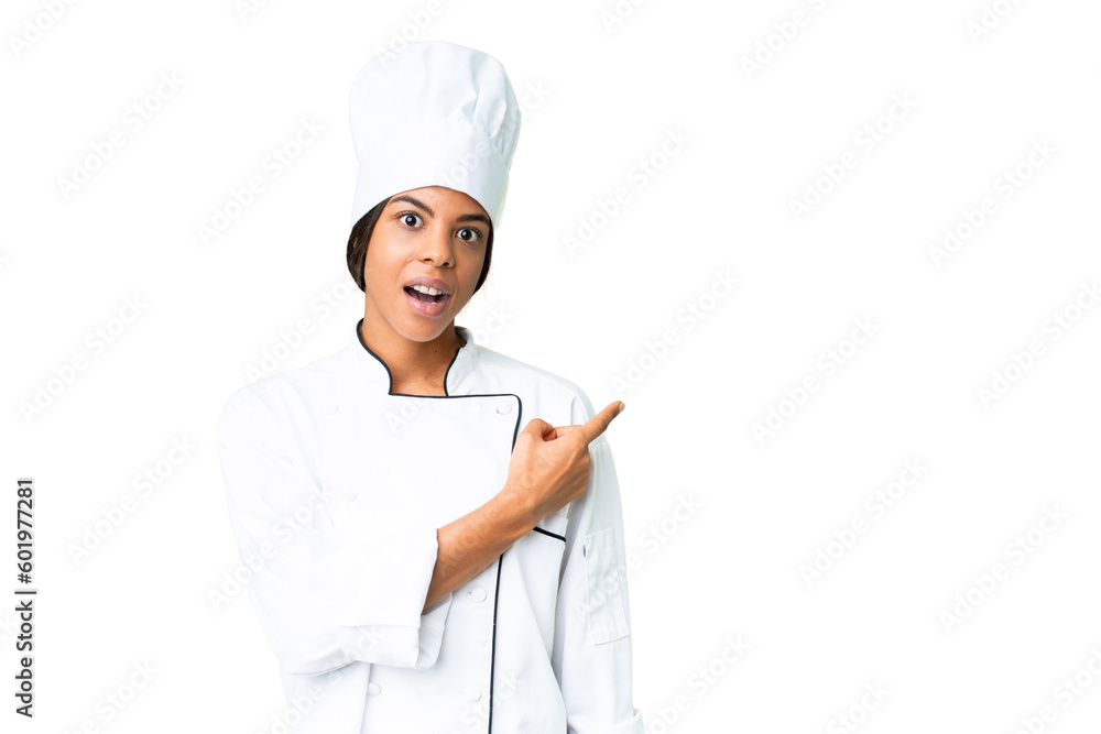 Young African American chef over isolated chroma key background surprised and pointing side Young African American chef over isolated chroma key background surprised and pointing side