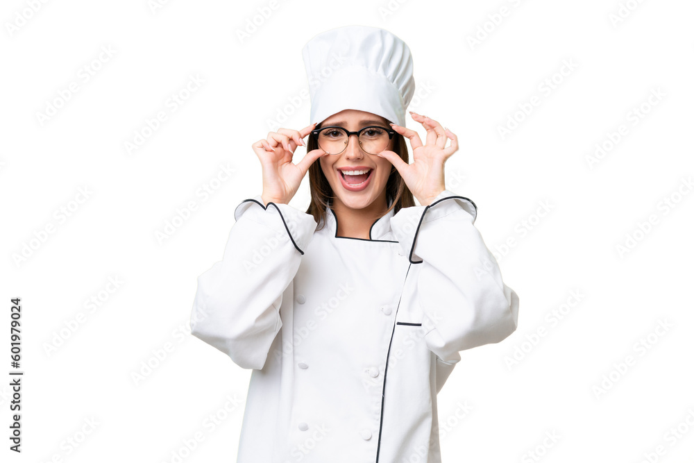 Young chef caucasian woman over isolated background with glasses and surprised Young chef caucasian woman over isolated background with glasses and surprised