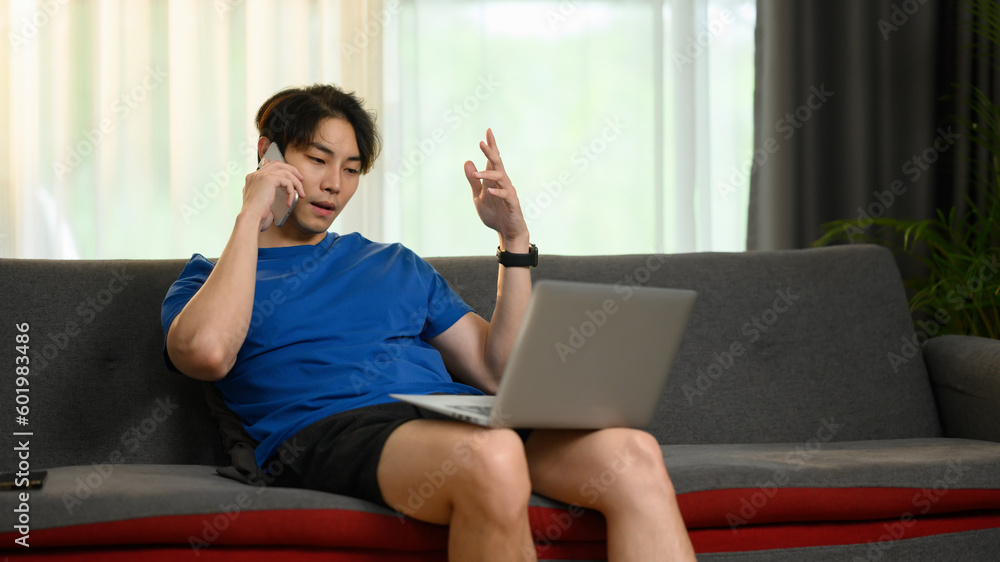 Image of Asian man freelancer using laptop and talking on mobile phone. Communication, people, technology concept Image of Asian man freelancer using laptop and talking on mobile phone. Communication, people, technology concept