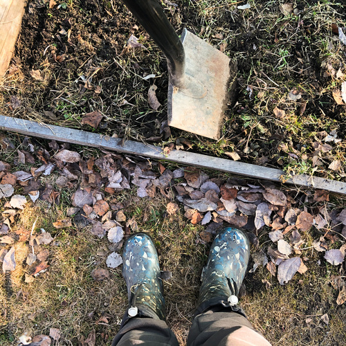 A gardener's feet in rubber boots and a shovel on a bed of soil