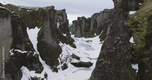 Flying Through Fjaðrárgljúfur Canyon Iceland on Cold WInter Day, Drone Shot of Volcanic Cliffs and Frozen Glacial Water 50fps photo