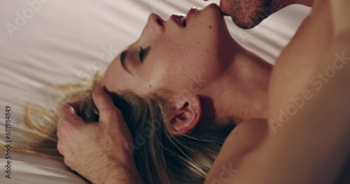 Couple, kissing and sex in home bedroom while erotic and sexual together. Man and a woman in bed for foreplay, libido and intimacy with a kiss on face for seduction, care and passion or desire