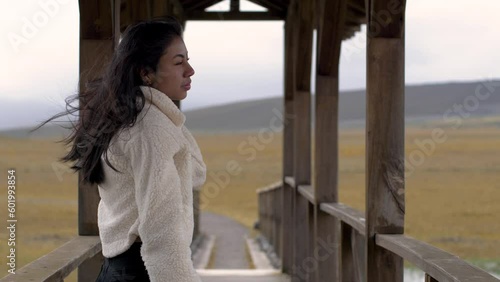 Medium view of woman fixing hair and walking to other side of bridge gazing out