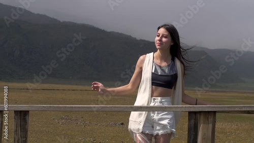 Girl in black crop top and white cardigan adjusts hair blowing in wind at cotopaxi national park