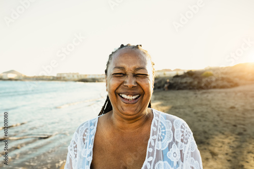 Happy African senior woman having fun smiling into the camera on the beach during summer vacation - Elderly people lifestyle concept