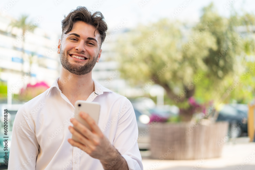 Young handsome man using mobile phone at outdoors with happy expression Young handsome man using mobile phone at outdoors with happy expression