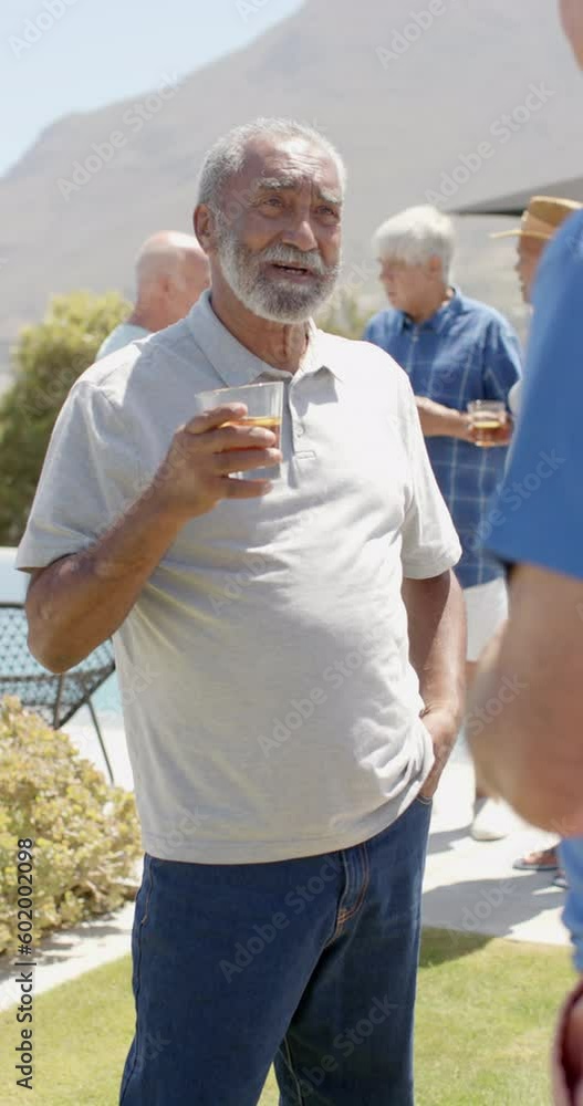 Happy senior diverse men talking and holding drinks in garden in slow motion Happy senior diverse men talking and holding drinks in garden in slow motion