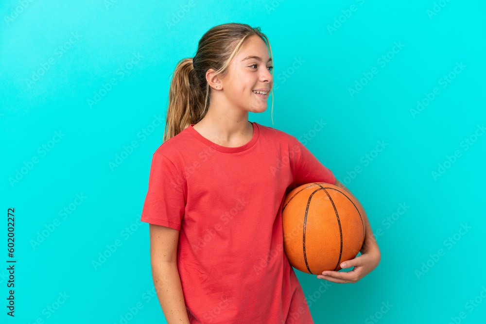 Little caucasian girl playing basketball isolated on blue background looking to the side and smiling Little caucasian girl playing basketball isolated on blue background looking to the side and smiling