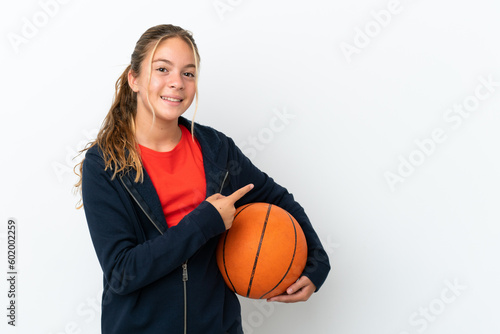 Little caucasian girl isolated on white background playing basketball and pointing to the lateral