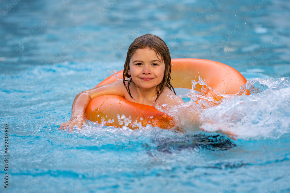 Happy child enjoying summer vacation outdoors in water in the swimming pool. Cute little kid in swimming suit relaxing on an inflatable ring. Kid floating in a pool.