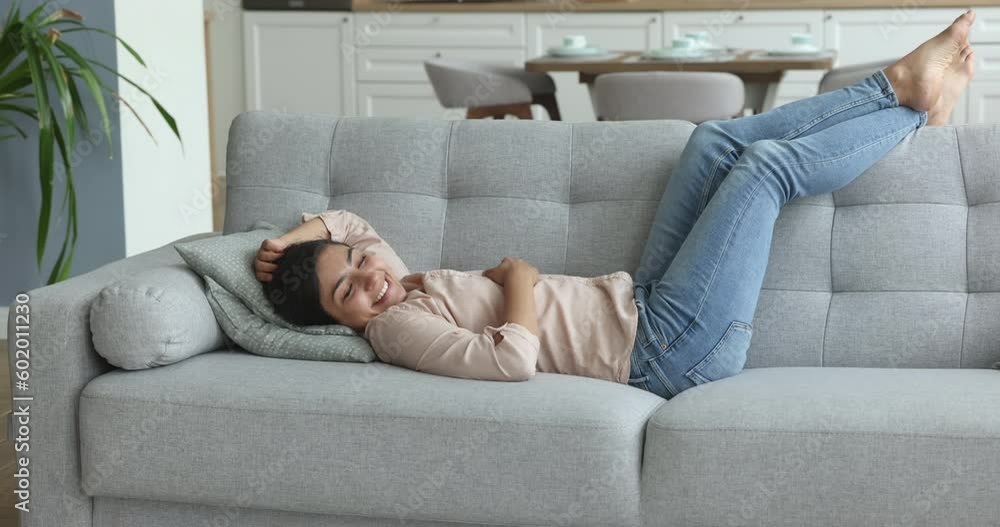 Calm Indian woman enjoy relaxation lying on cozy comfortable sofa in living room of modern studio apartment. Fatigue relief, lazy weekend leisure at home. Rest, repose, day off, climate control inside Calm Indian woman enjoy relaxation lying on cozy comfortable sofa in living room of modern studio apartment. Fatigue relief, lazy weekend leisure at home. Rest, repose, day off, climate control inside