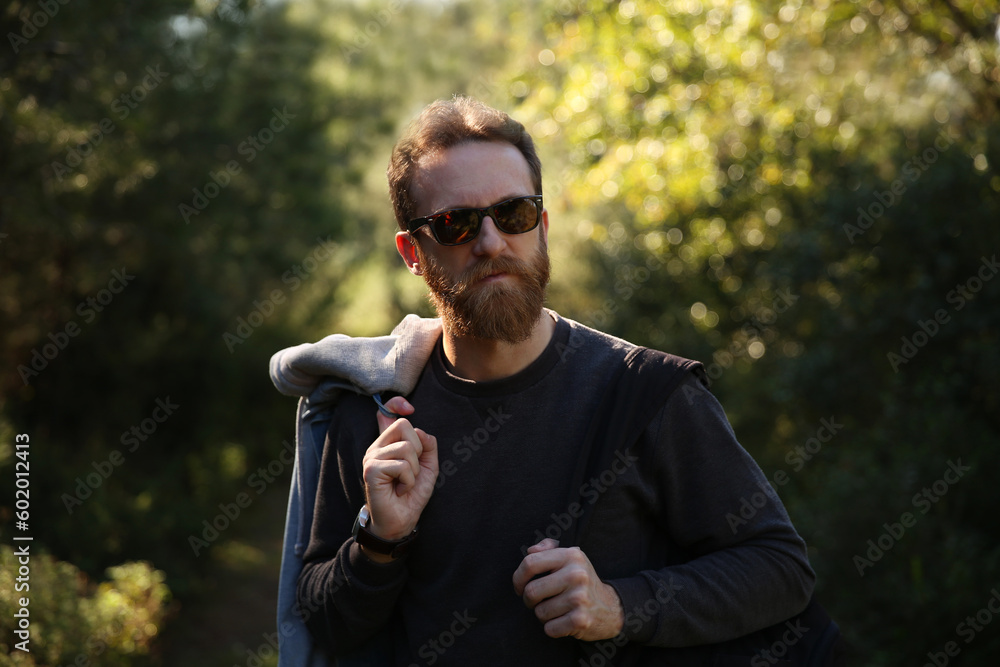 Trekking lover, adventurer, bearded Caucasian man with sunglasses posing in front of a blurry background with soft natural light Trekking lover, adventurer, bearded Caucasian man with sunglasses posing in front of a blurry background with soft natural light