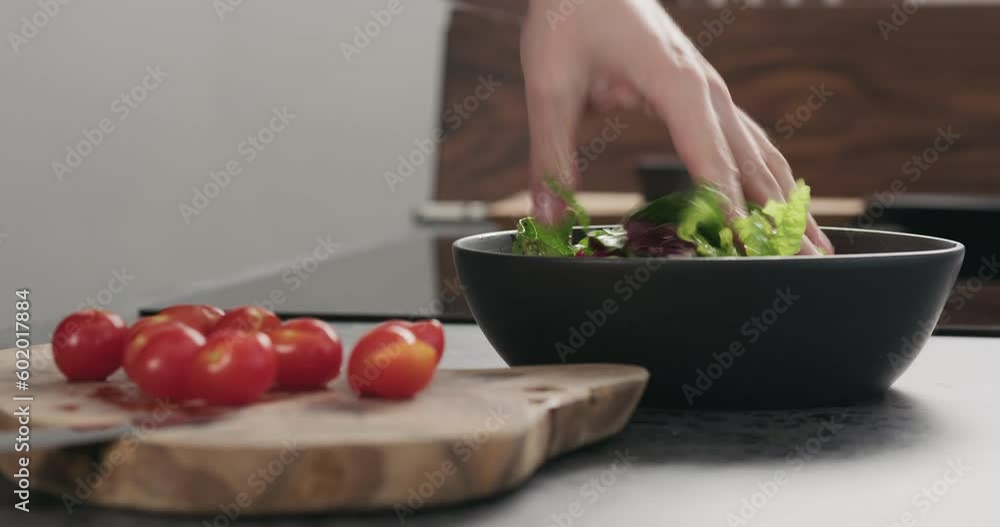 Closeup man making salad with greens , tomatoes and steak in a black bowl Closeup man making salad with greens , tomatoes and steak in a black bowl