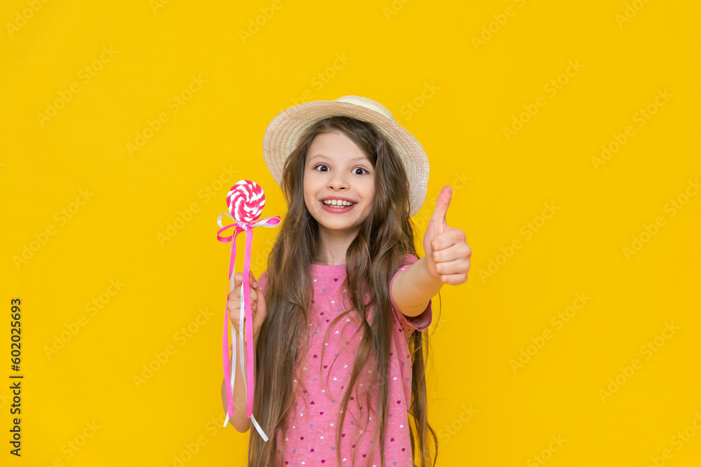 A little sweet tooth in a straw hat with a lollipop on a stick. A child holds sweets and candies in his hand, an orange background model with a lollipop on a stick on an isolated background. A little sweet tooth in a straw hat with a lollipop on a stick. A child holds sweets and candies in his hand, an orange background model with a lollipop on a stick on an isolated background.