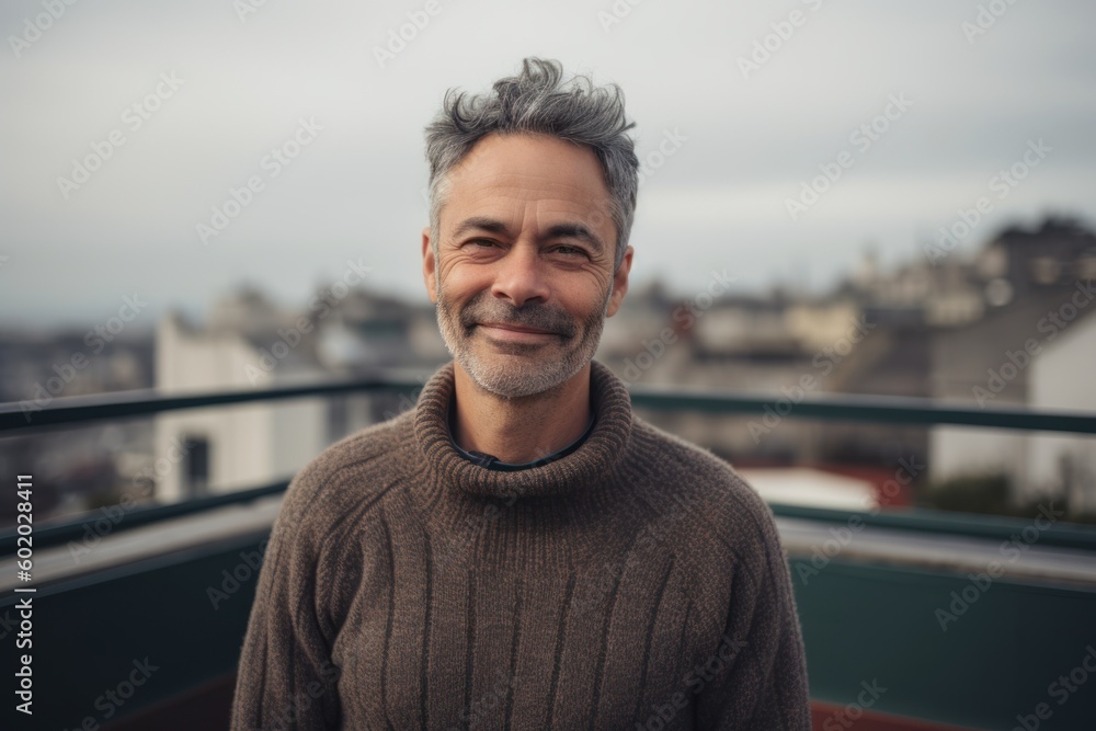 Fototapeta premium Portrait of a handsome middle-aged man with gray hair, wearing a woolen sweater, standing on the roof of a building.