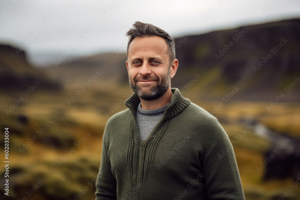 Portrait of a handsome bearded man in a green sweater standing in the middle of a volcanic landscape